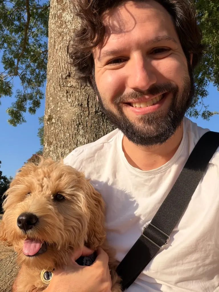 Luca, who has dark curly hair and a beard, holding Copper under a tree